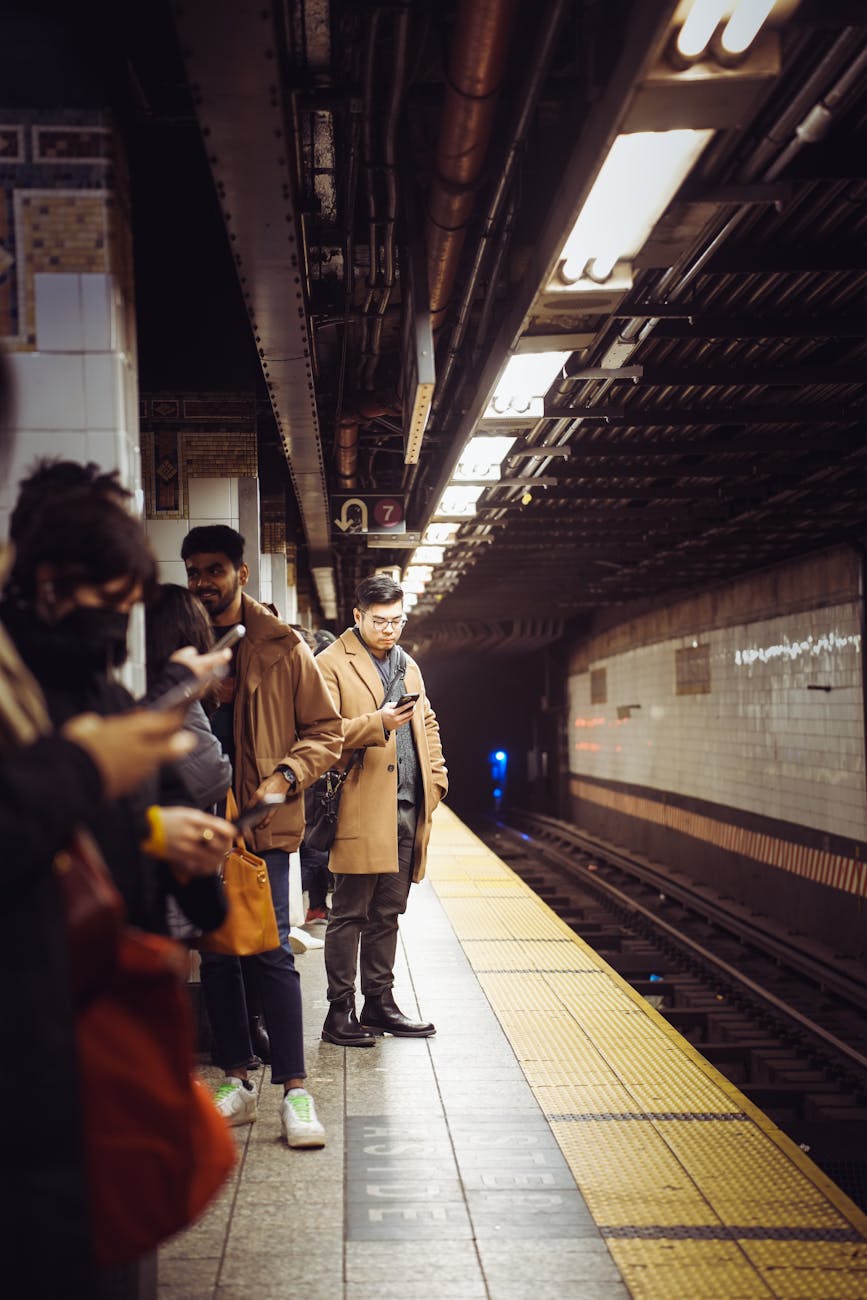 Commuters use smartphones while waiting at a subway station. Urban transit scene.