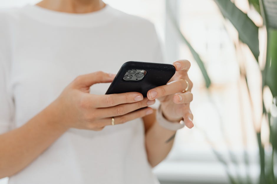 Close-up of woman holding a smartphone, casually browsing indoors with natural light.