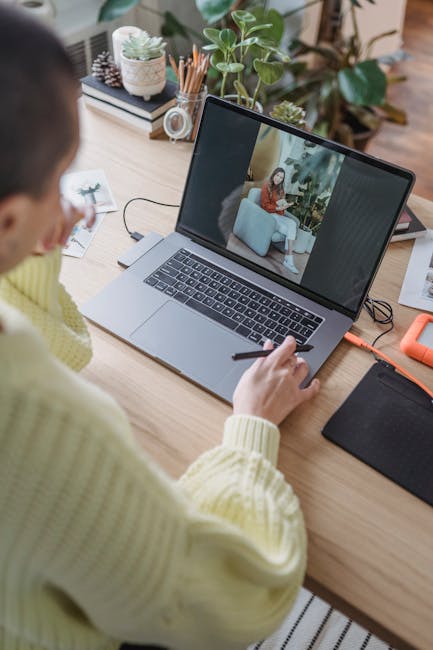 An adult woman editing photos on a laptop in a modern indoor workspace with plants and office supplies.